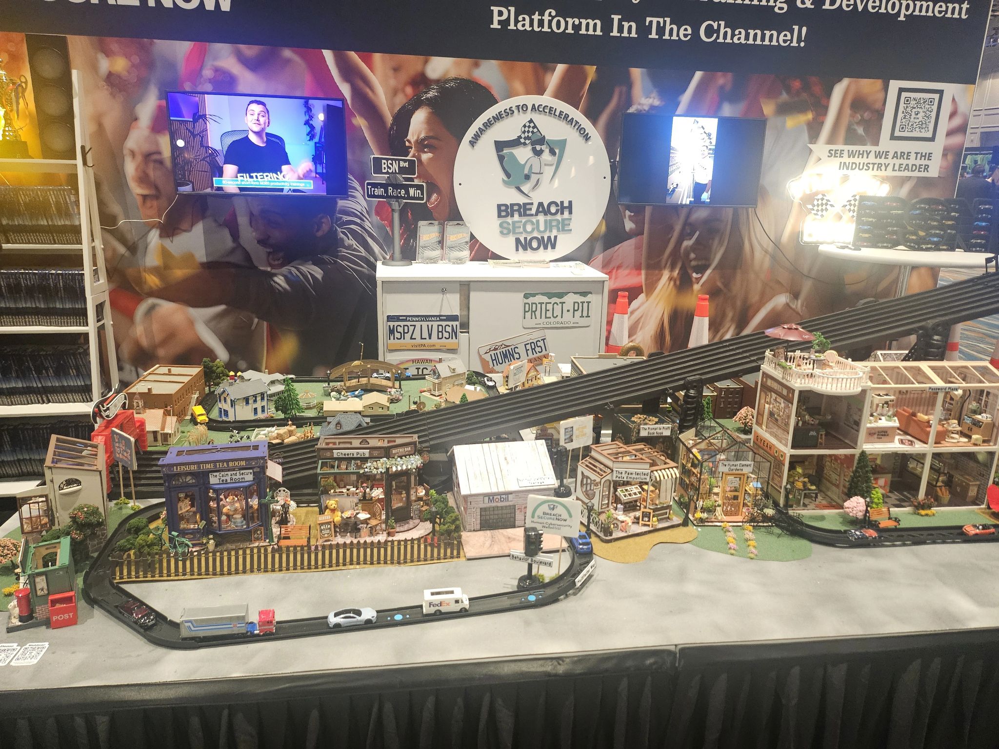 The City of BSN booth at IT Nation Connect 2025: a handmade miniature city with a toy racetrack in front of the Breach Secure Now backdrop