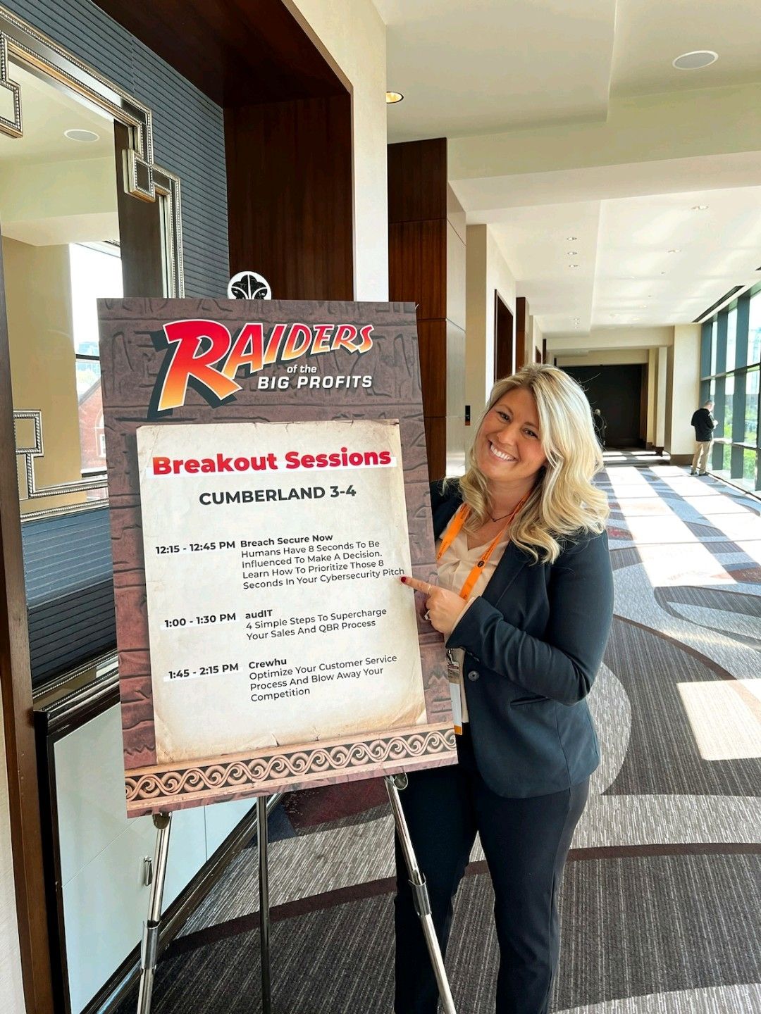 Tracie Crites beside the breakout sessions board listing her Breach Secure Now session, Nashville, 2023