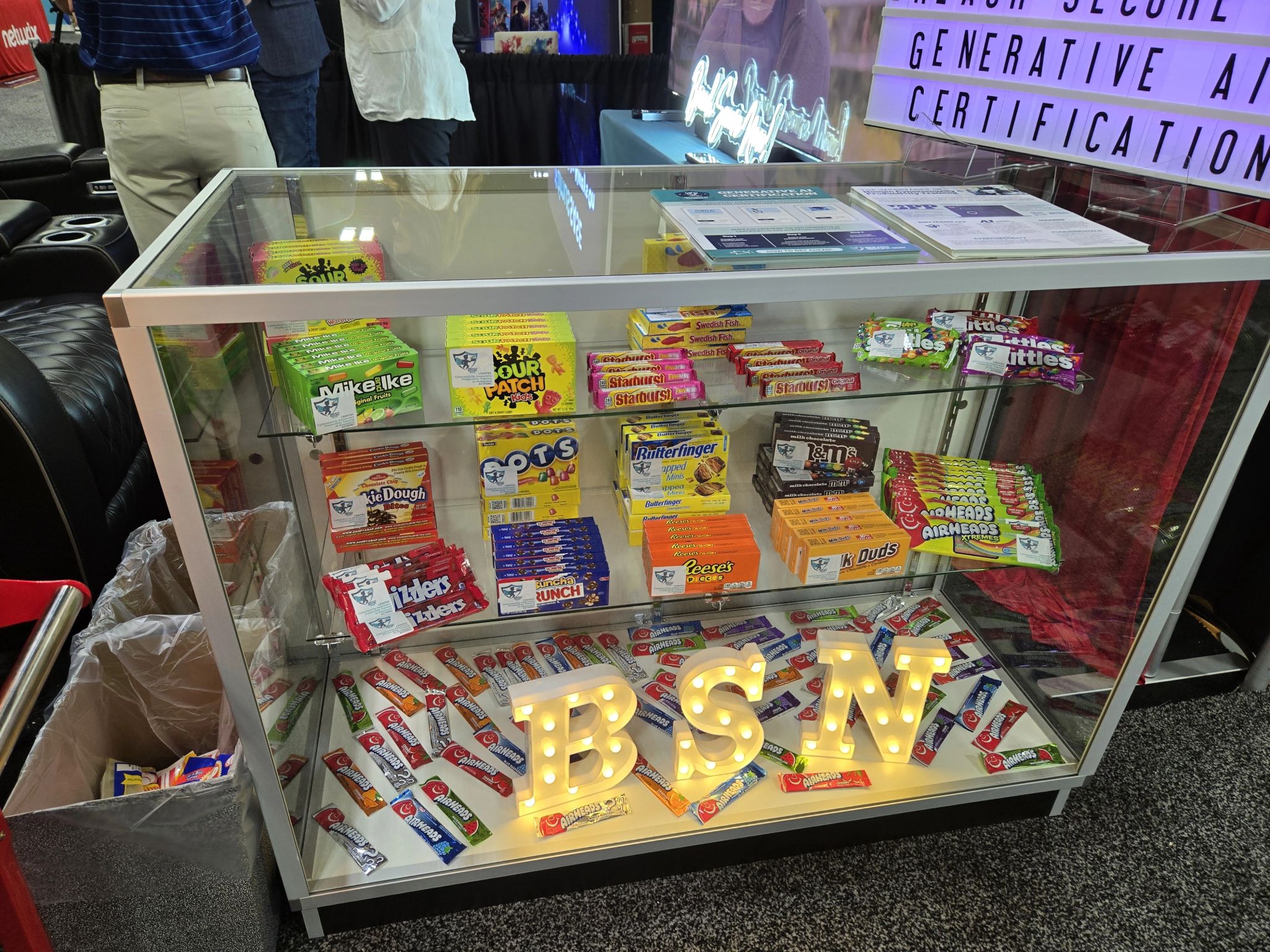 The movie-lounge booth at Pax8 Beyond 2025: a glass candy case of Breach Secure Now boxes above lit BSN letters